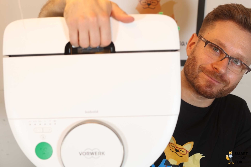 Der Vorwerk Kobold VR7 wird mit Hilfe des Tragegriffs hochgehalten.